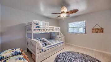 A child's bedroom with bunk beds, a ceiling fan, a window with blinds, and a patterned rug.