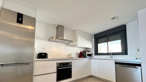 Et moderne køkken med rustfrie hårde hvide elementer og et vindue med persienner.