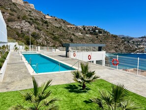 A swimming pool with a lifebuoy, a grassy area, and a view of a coastal town. - Apartment "Icon Marina A" with Sea Views, Shared Pool and Wi-Fi (La Herradura)