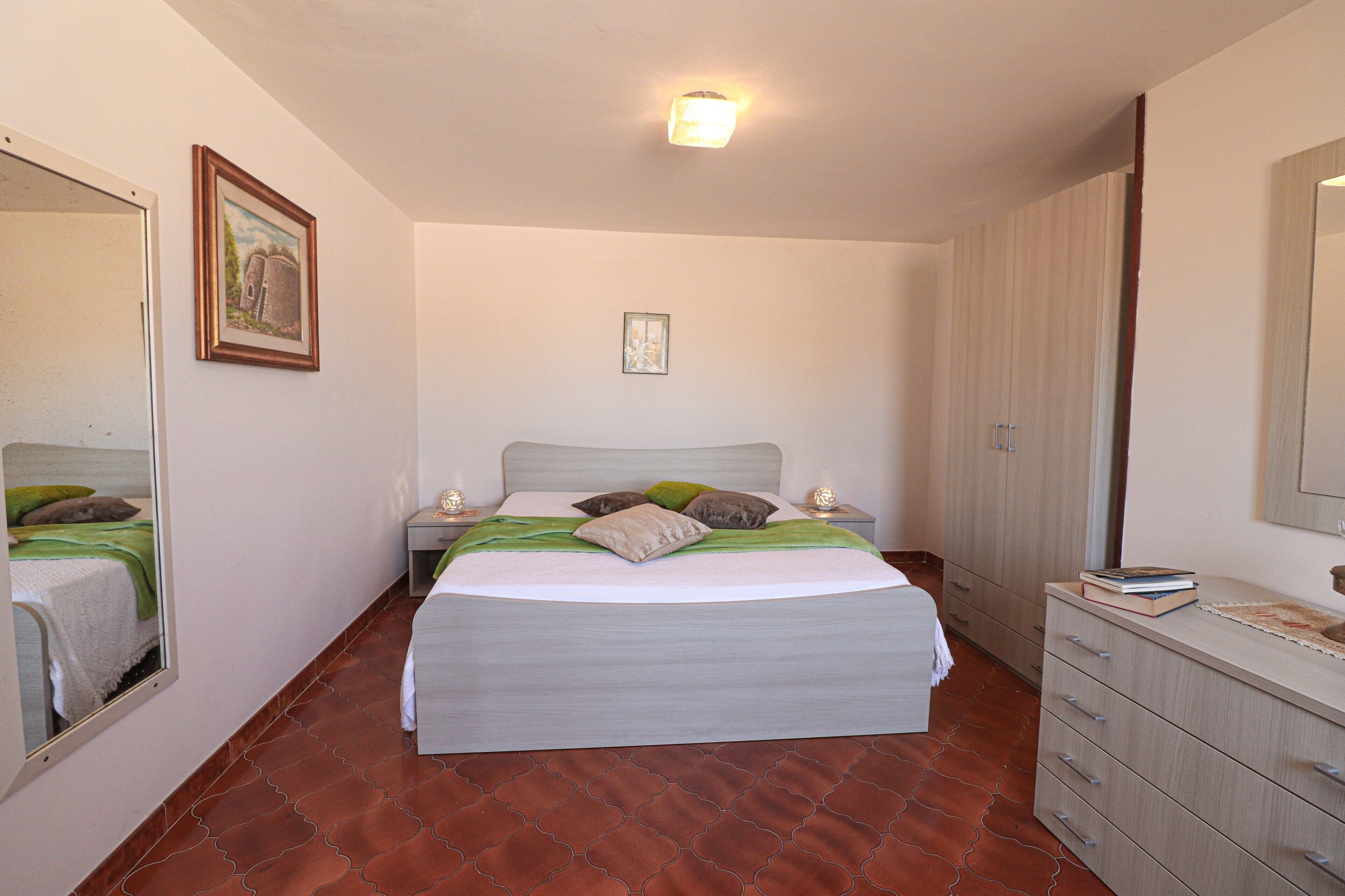 A bedroom with a bed, bedside tables, a dresser, a mirror, and a framed picture on the wall.