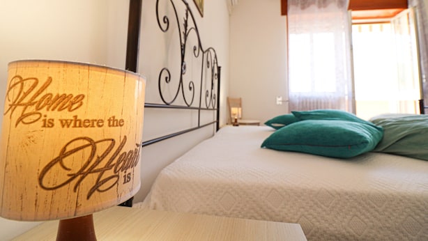 Un dormitorio con una cama, una lámpara de pared y un ventanal con cortinas.