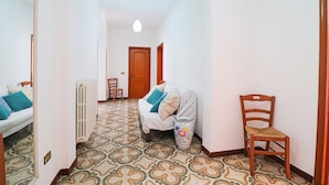 Un pasillo con baldosas estampadas, un radiador, un sofá con cojines, una silla y una puerta de madera.