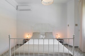 Un dormitorio con una cama blanca, dos mesitas de noche con lámparas, un equipo de aire acondicionado blanco y una alfombra con textura.