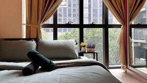 Un dormitorio con cama, almohadas, una mesita de noche con un jarrón de flores y cortinas.