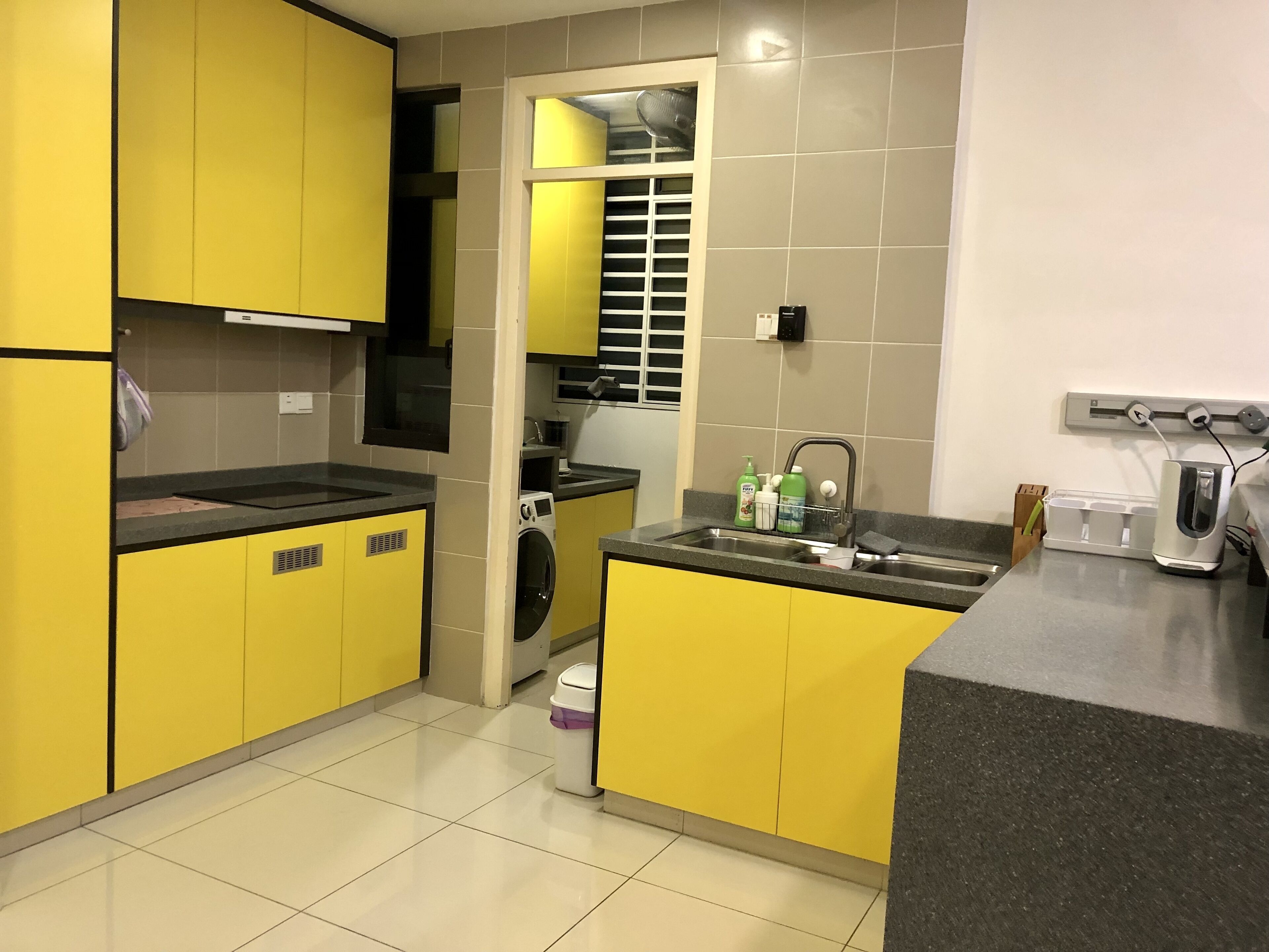 A compact kitchen with yellow cabinets, a built-in washing machine, a sink with a soap dispenser, and a countertop with a coffee maker.