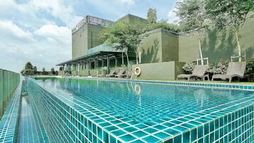 Ein Pool mit Fliesenrand, umgeben von Liegestühlen und einem Gebäude mit grüner Fassade.