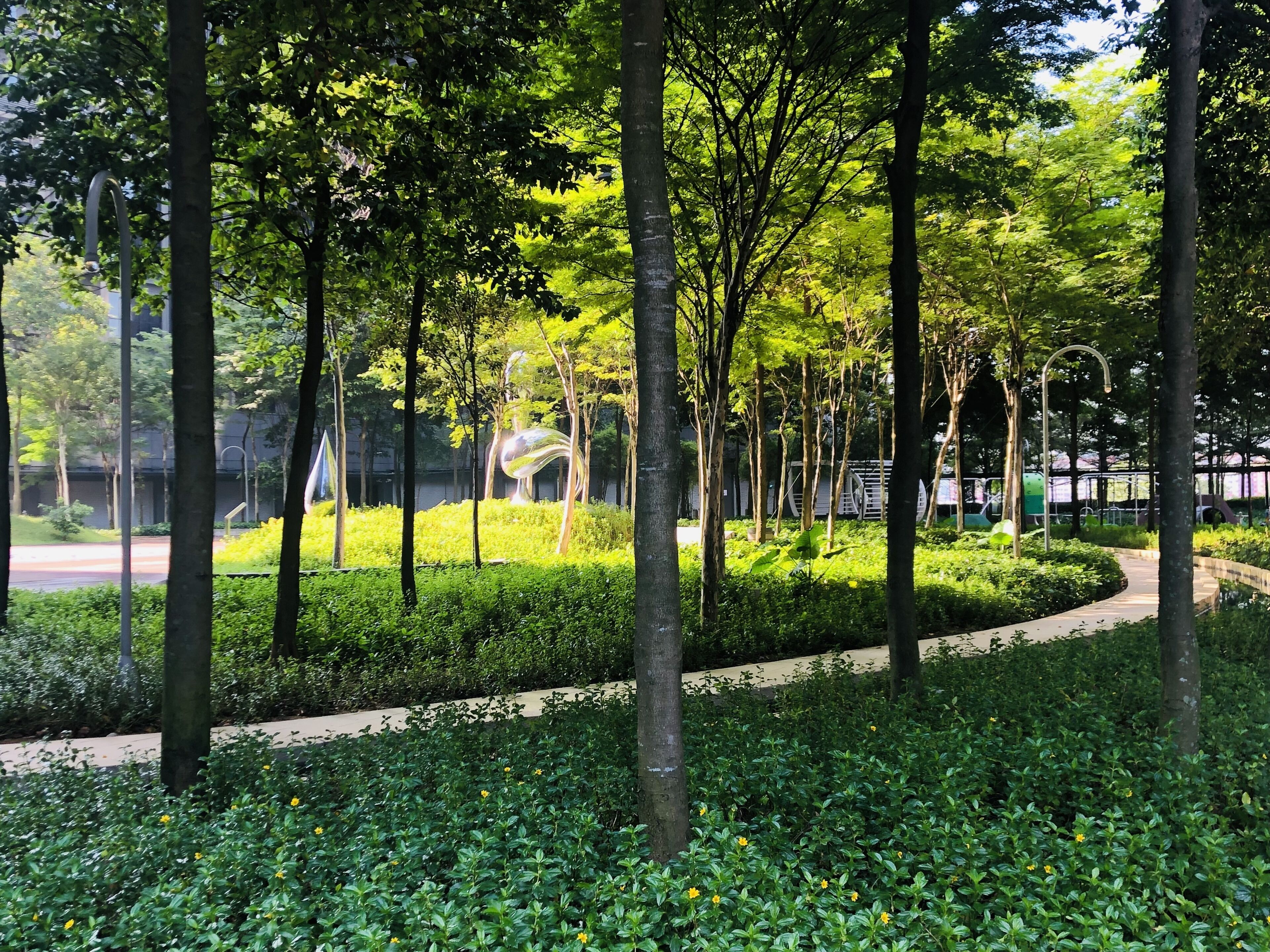 A park with trees, a curved pathway, and a metal sculpture.