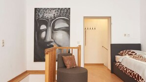 A bedroom with a bed, a chair, a large artwork, and a door.