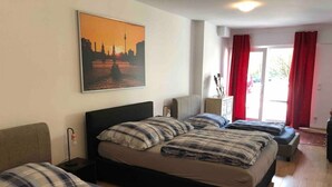 A hotel room with a large bed, two smaller beds, a painting of a cityscape, and a view of the outdoors through a window. - Potsdamer Platz-Top Spot Studio 1 (Berlin)
