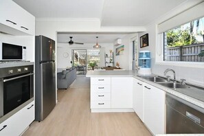 Una cocina moderna con armarios blancos, electrodomésticos de acero inoxidable y un amplio ventanal.
