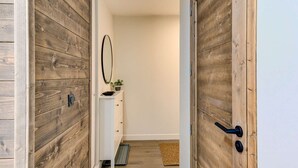 Un pasillo con puertas de madera, un armario blanco, un espejo y una planta pequeña.
