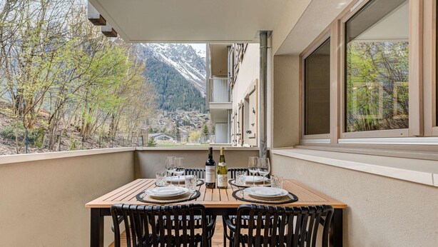 Un balcón con una mesa de madera dispuesta para comer, con vistas a un paisaje montañoso.