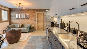 Una cocina moderna con horno integrado, pileta y encimera. Se aprecia una pared de madera y una ventana con vista al exterior.