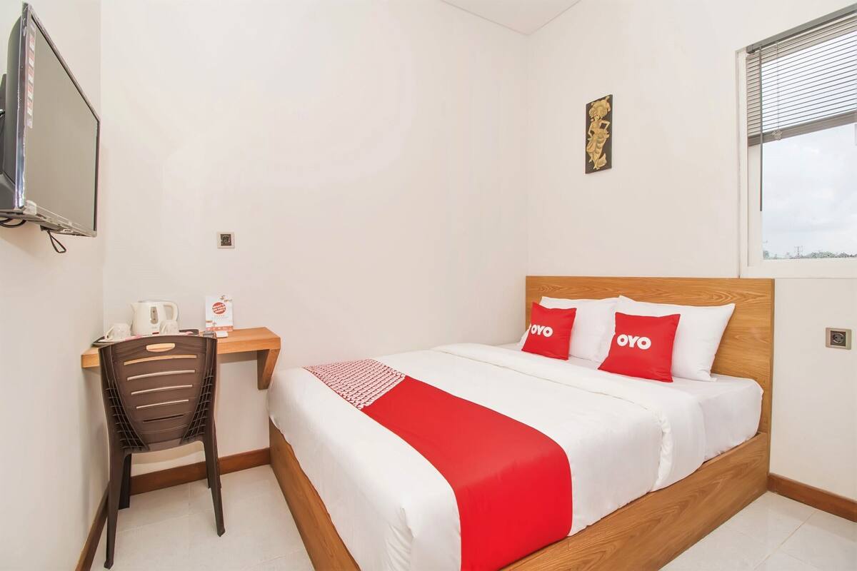 Une chambre d’hôtel avec un lit, un bureau, une chaise, une télévision et une fenêtre.