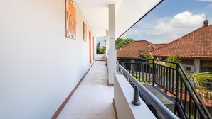 A corridor with a tiled floor, white walls, and a balcony with a metal railing.