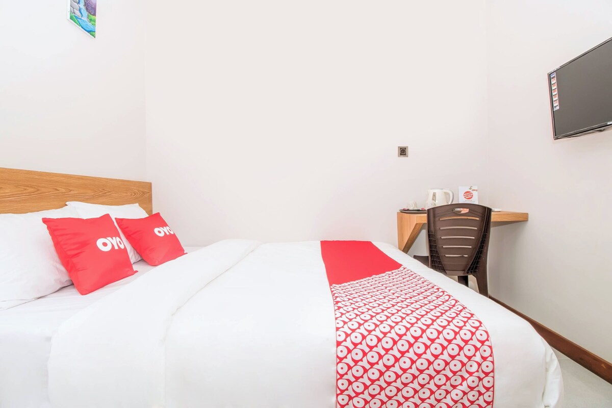 Een hotelkamer met een bed, een bureau, een stoel, een televisie en een wandplank.