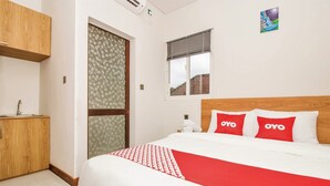 A hotel room with a bed, a wooden wardrobe, a bathroom with a toilet, and a window with a view of buildings.