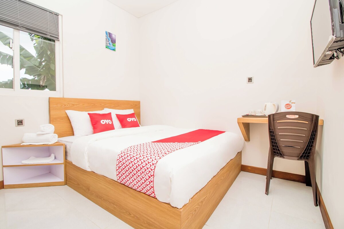 A neatly made bed with a red and white patterned blanket, a wooden headboard, and a small bedside table with a white towel.