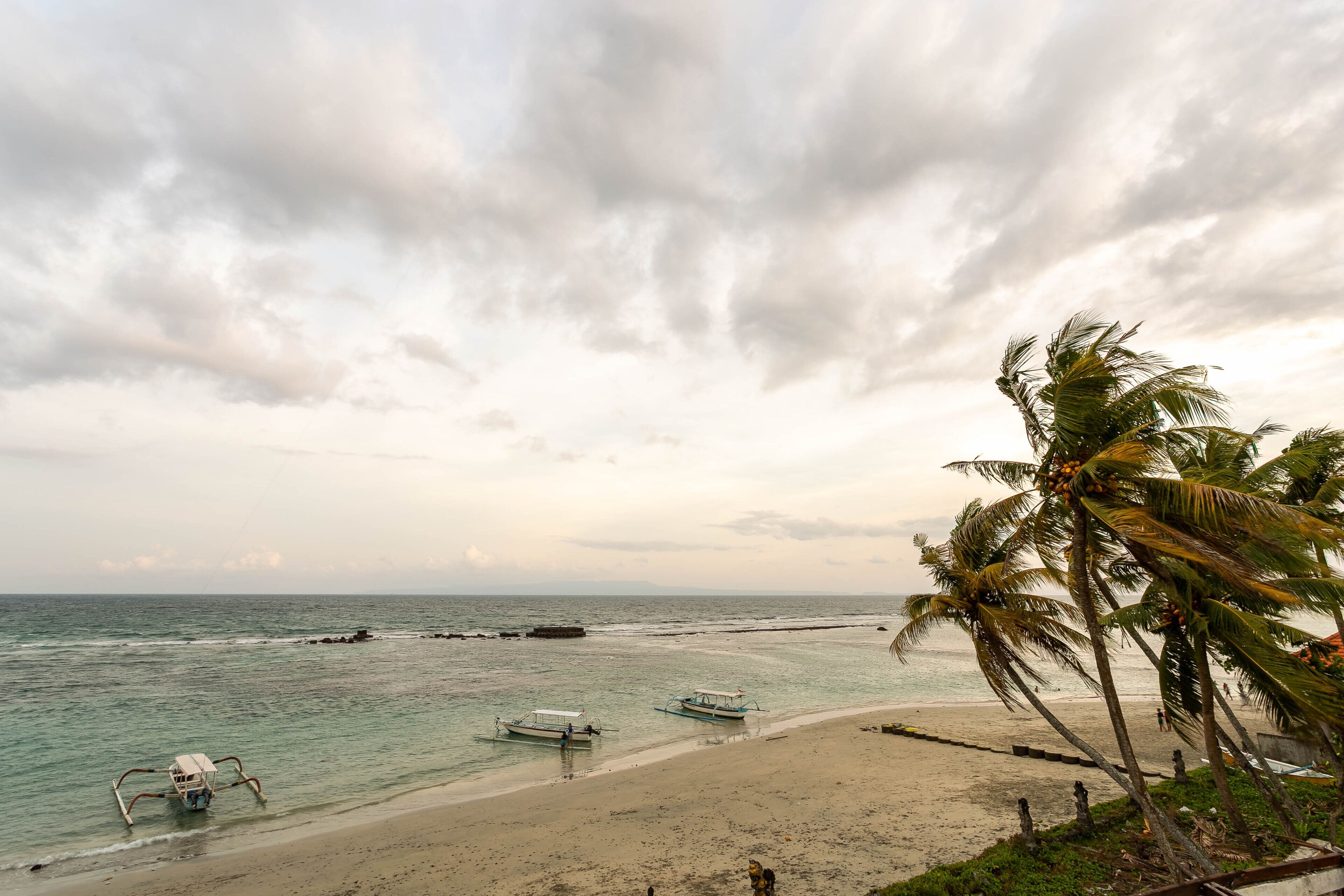 Uma praia com barcos, palmeiras e um céu nublado.