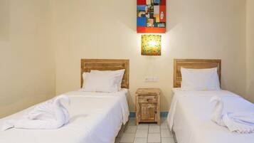 Habitación de hotel con dos camas individuales, cada una con cabecero de madera y ropa de cama blanca. Hay una mesita de noche de madera entre las camas, y una obra de arte colorida se exhibe sobre la mesita.