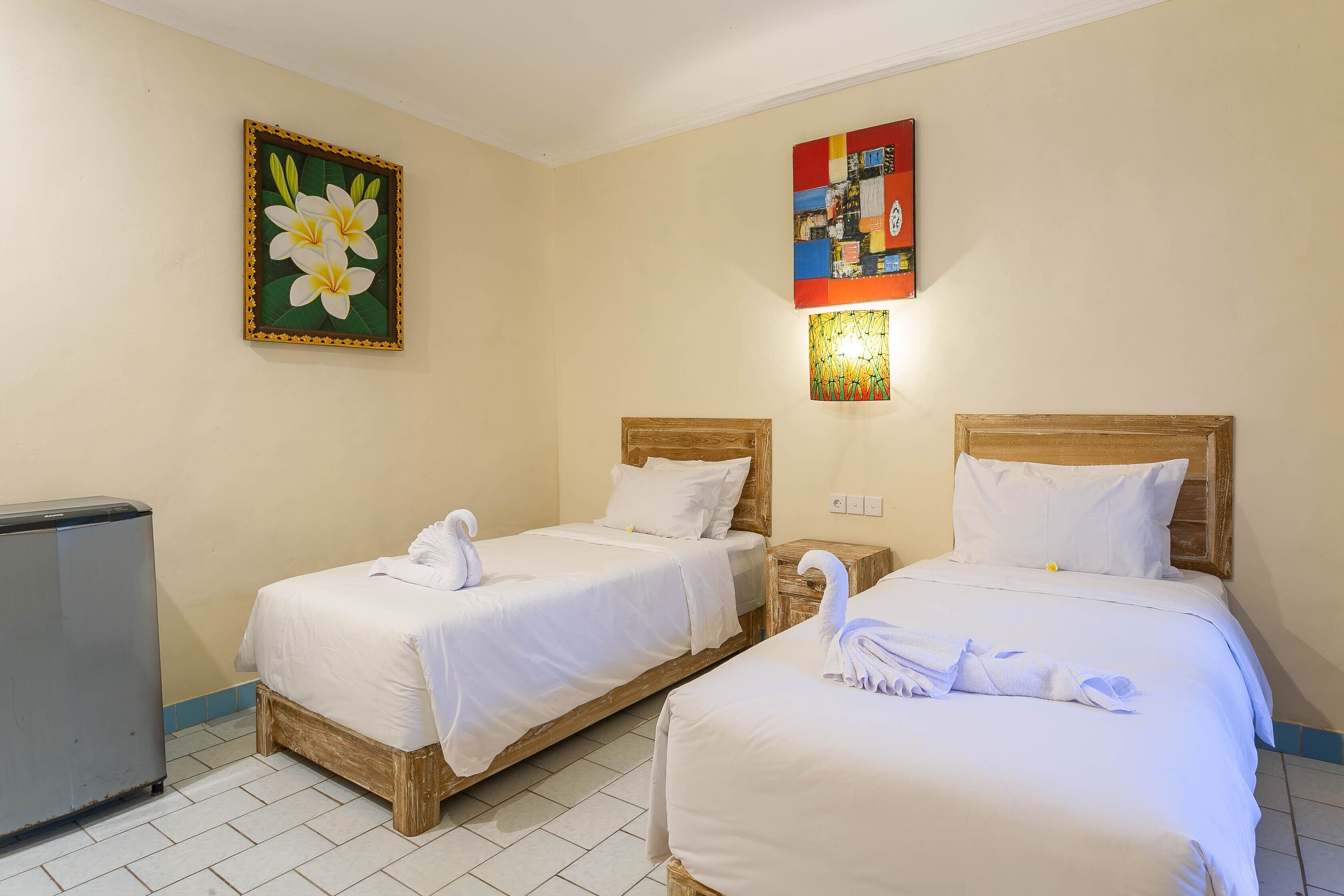 Une chambre d’hôtel avec deux lits simples, un petit réfrigérateur et un tableau au mur.