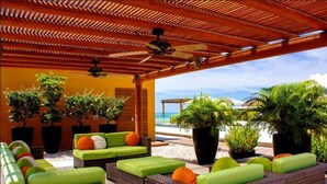 A covered outdoor seating area with wicker furniture and green cushions, overlooking a beach. - Gorgeous 1 Bedroom Unit at V399, amazing Rooftop 1BD Condo for rent in Old Town, (Puerto Vallarta)