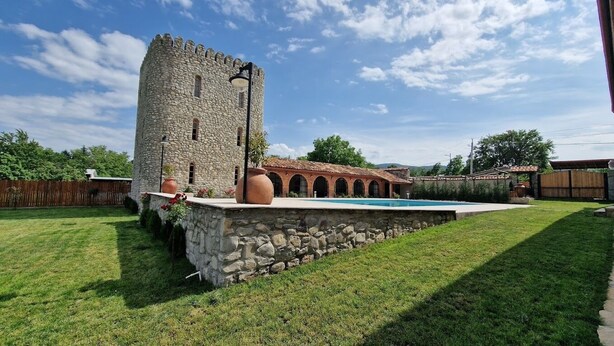 Una torre de piedra, una piscina y un edificio con ventanales arqueados.