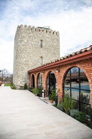 A stone tower with a brick building in front. - Giorgi Ushikishvili Chateau Celler (Akhmeta)