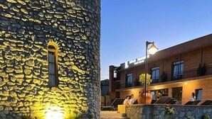 A stone building with a balcony, a grassy area with a blanket and candles, and a modern building in the background.