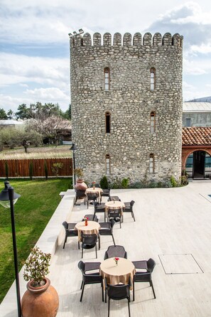 A stone castle with a courtyard featuring outdoor seating and a large vase. - Giorgi Ushikishvili Chateau Celler (Akhmeta)