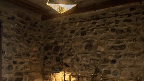 A room with two beds, stone walls, and a hanging light fixture.