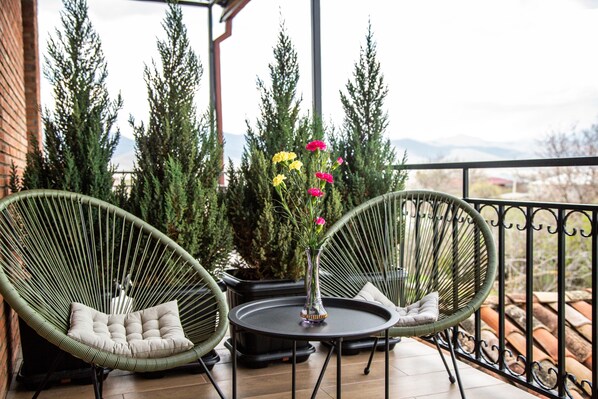 A balcony with two green wicker chairs, a small round table, and a vase with flowers.