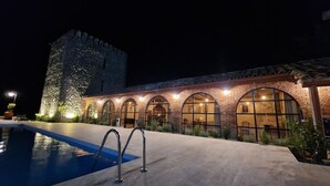 Un hotel con piscina, ventanas arqueadas y una torre de piedra.