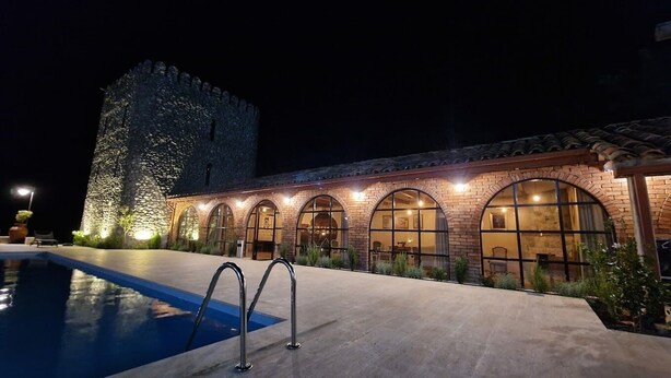 A hotel with a swimming pool, arched windows, and a stone tower.