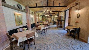 A restaurant with stone flooring, wooden beams, and brick walls. Tables and chairs are arranged for dining.