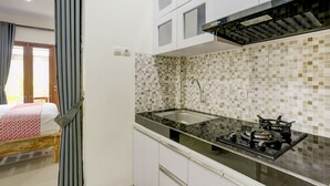 Una cocina compacta con estufa a gas, alacenas blancas y salpicadero de azulejos.
