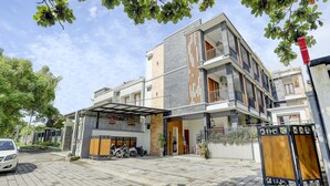 Un edificio residencial moderno de varios pisos con un acceso cubierto, una zona de estacionamiento cerrada y un coche blanco estacionado afuera.