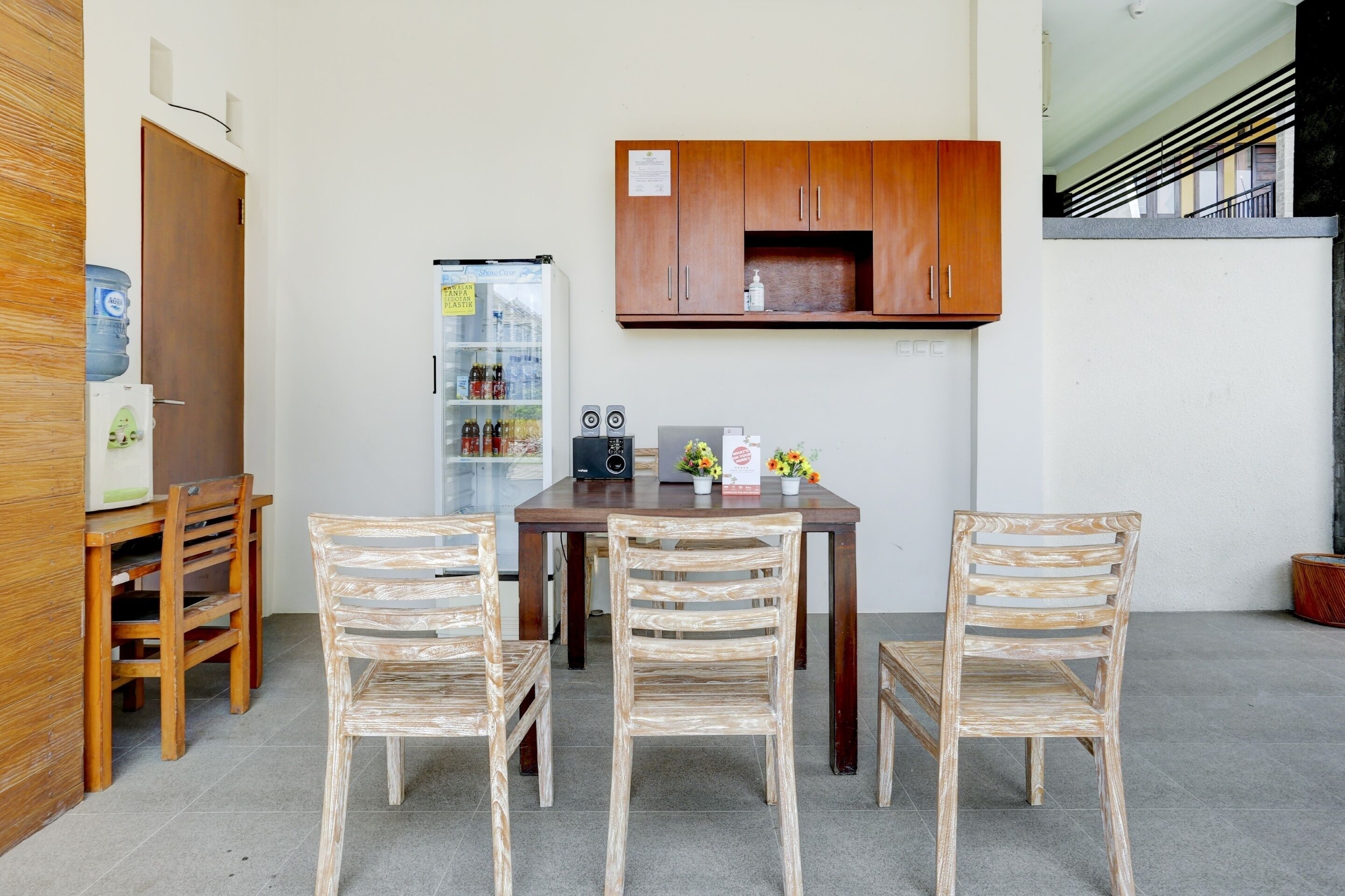 A small dining area with a wooden table and four chairs, a refrigerator, a water dispenser, and a cabinet above the table.