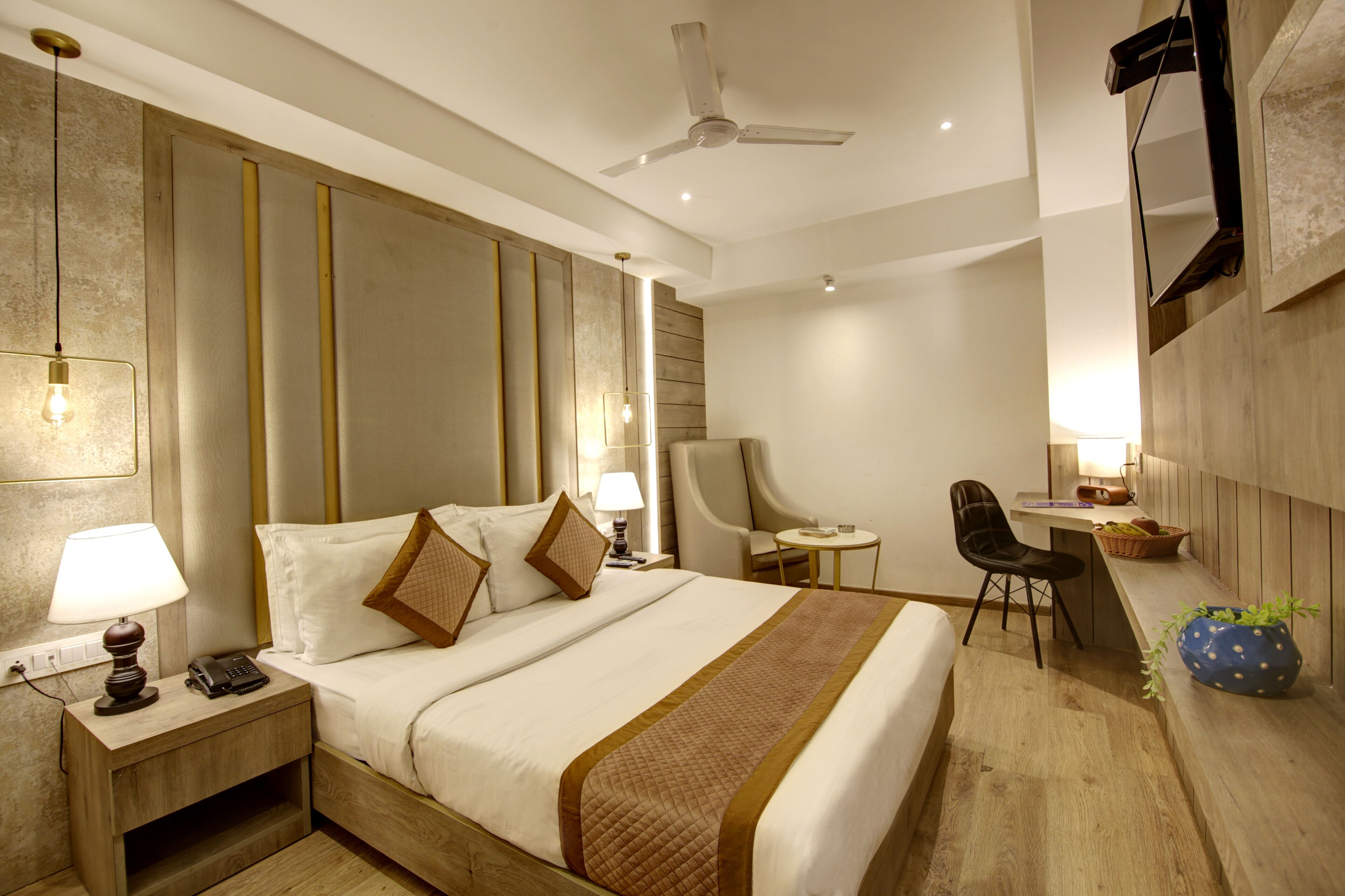 Habitación de hotel con una cama grande, mesita de noche con lámpara, escritorio con silla y ventilador de techo.