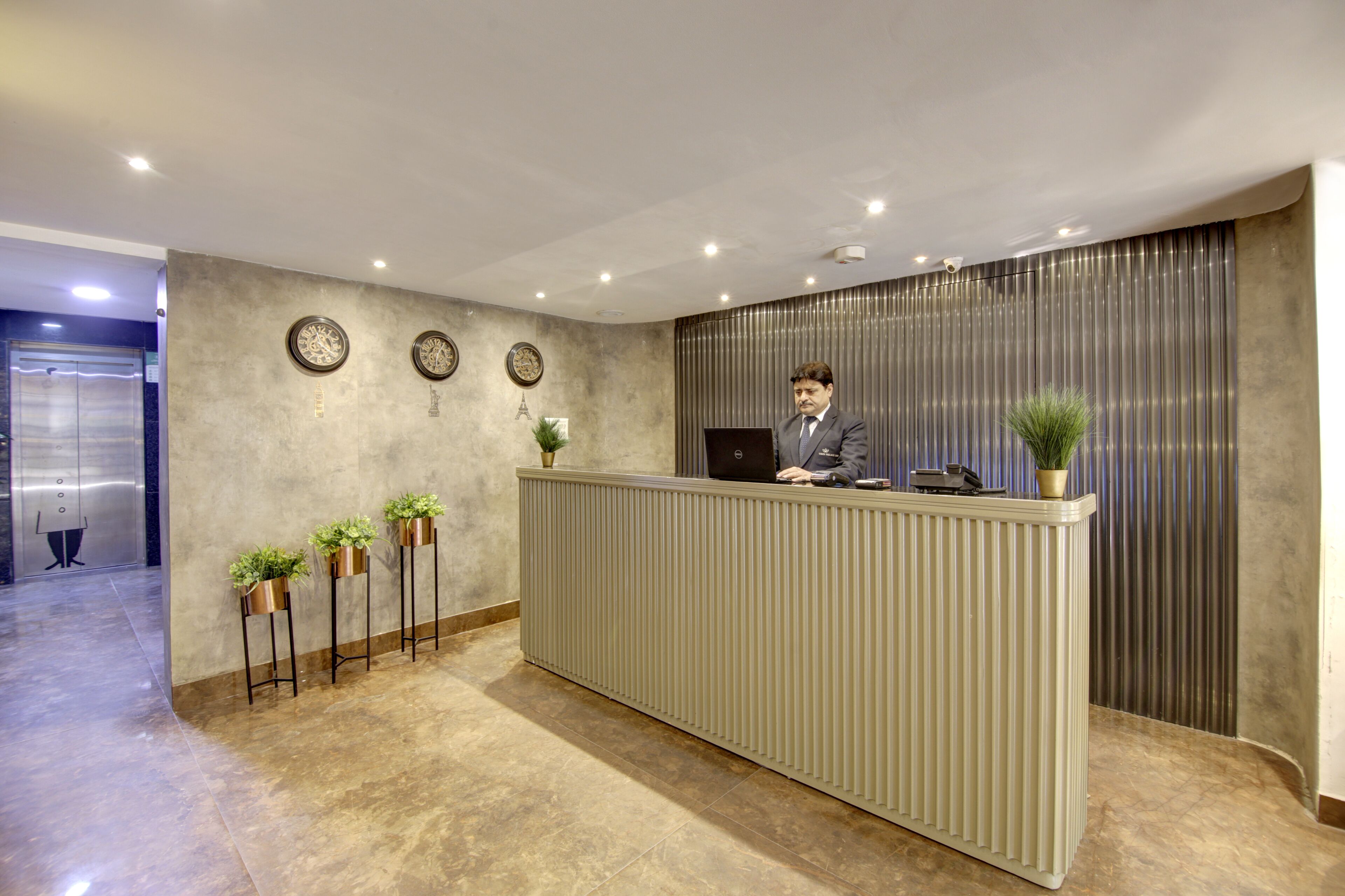 Una recepción de diseño moderno, con superficie plana y una planta en maceta. Se ven tres relojes de pared sobre el mostrador, y una cortina vertical a la derecha.