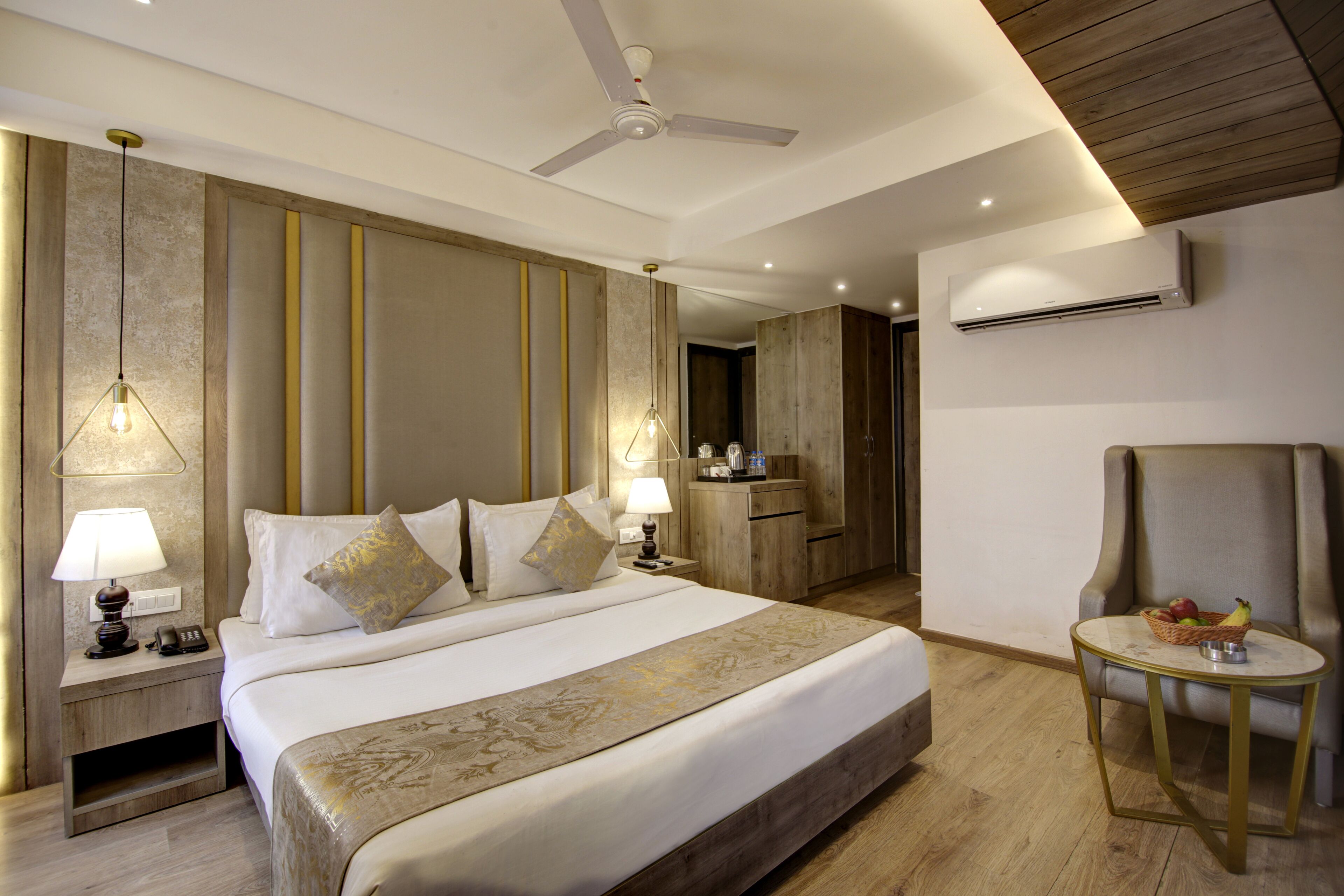A hotel room with a large bed, bedside lamps, a desk, a chair, and an air conditioning unit.