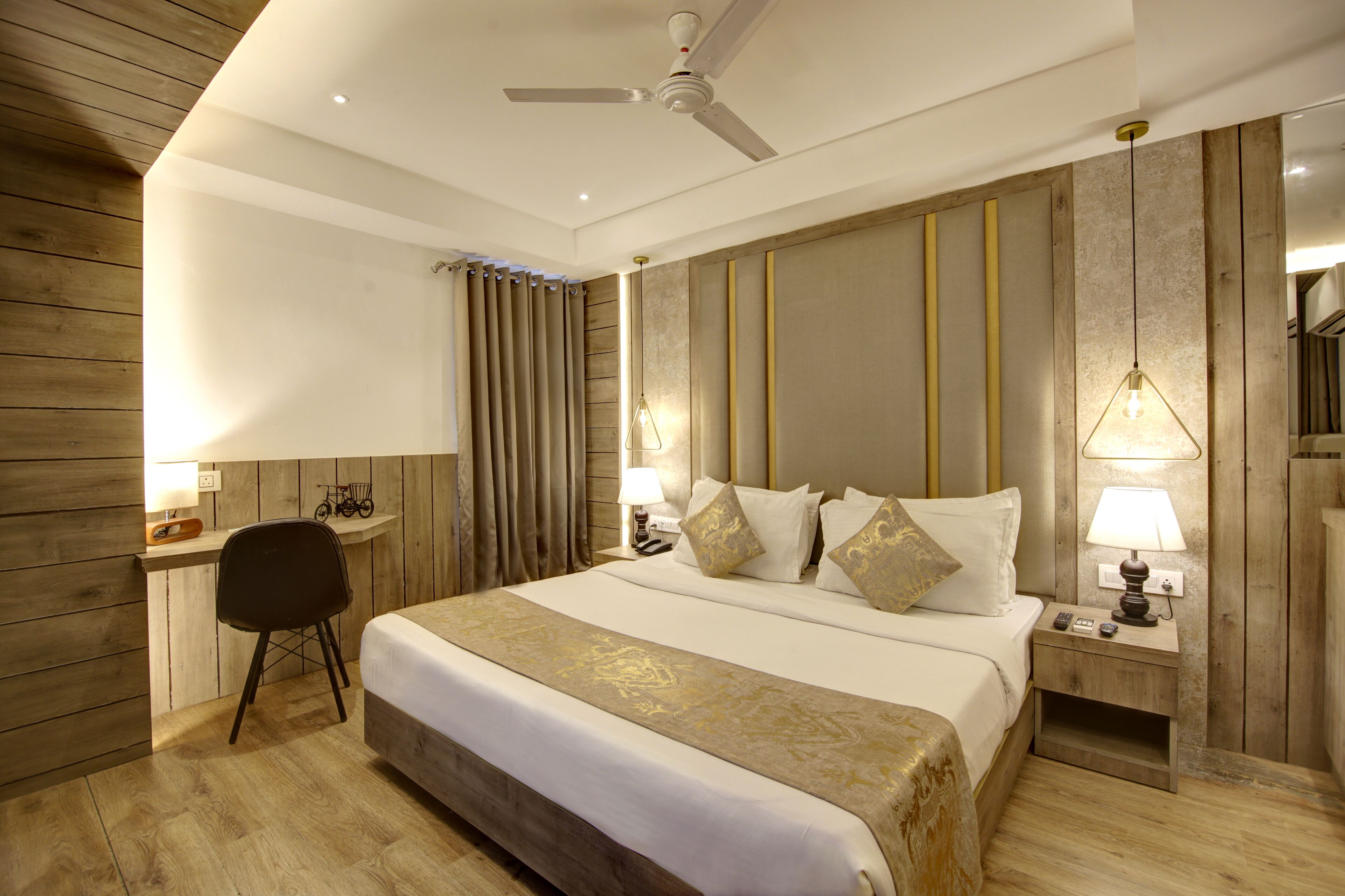 A hotel room with a large bed, two bedside tables with lamps, a desk with a chair, and a ceiling fan.