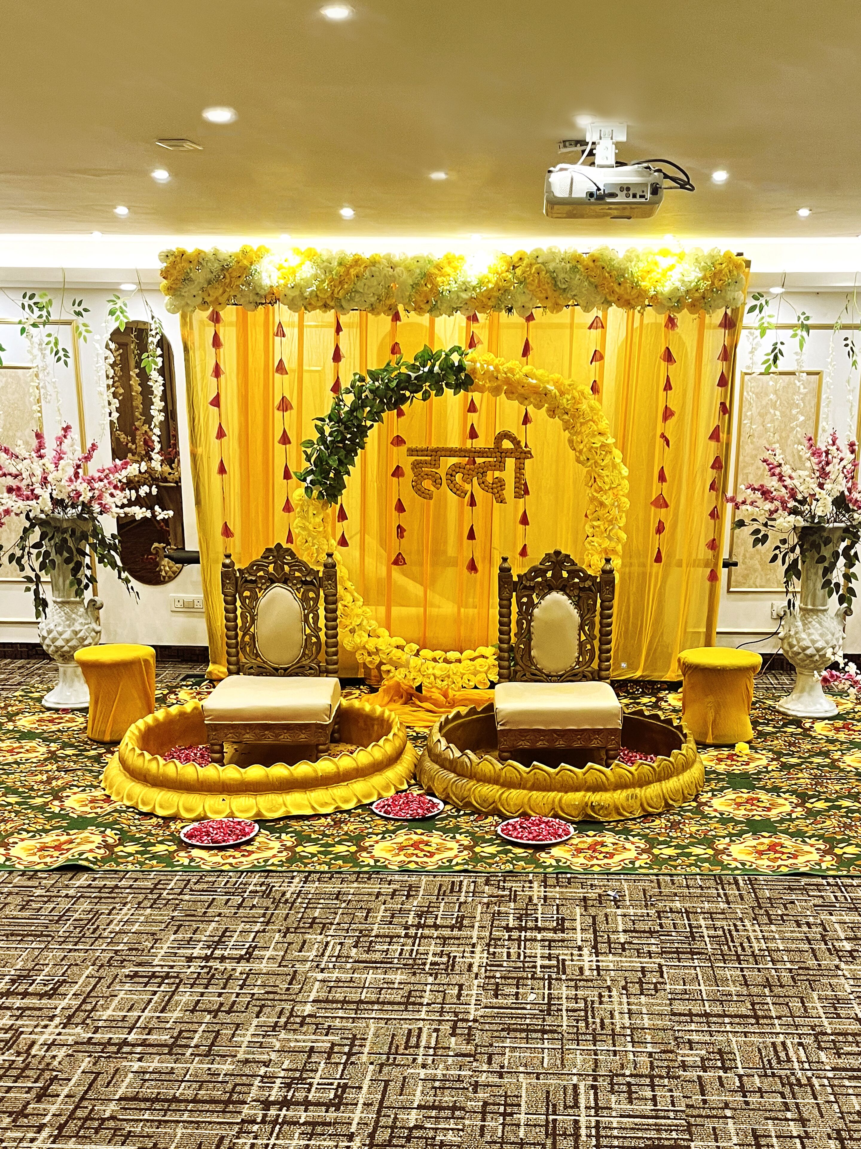 A stage with yellow curtains and floral decorations, two chairs, and a projector.