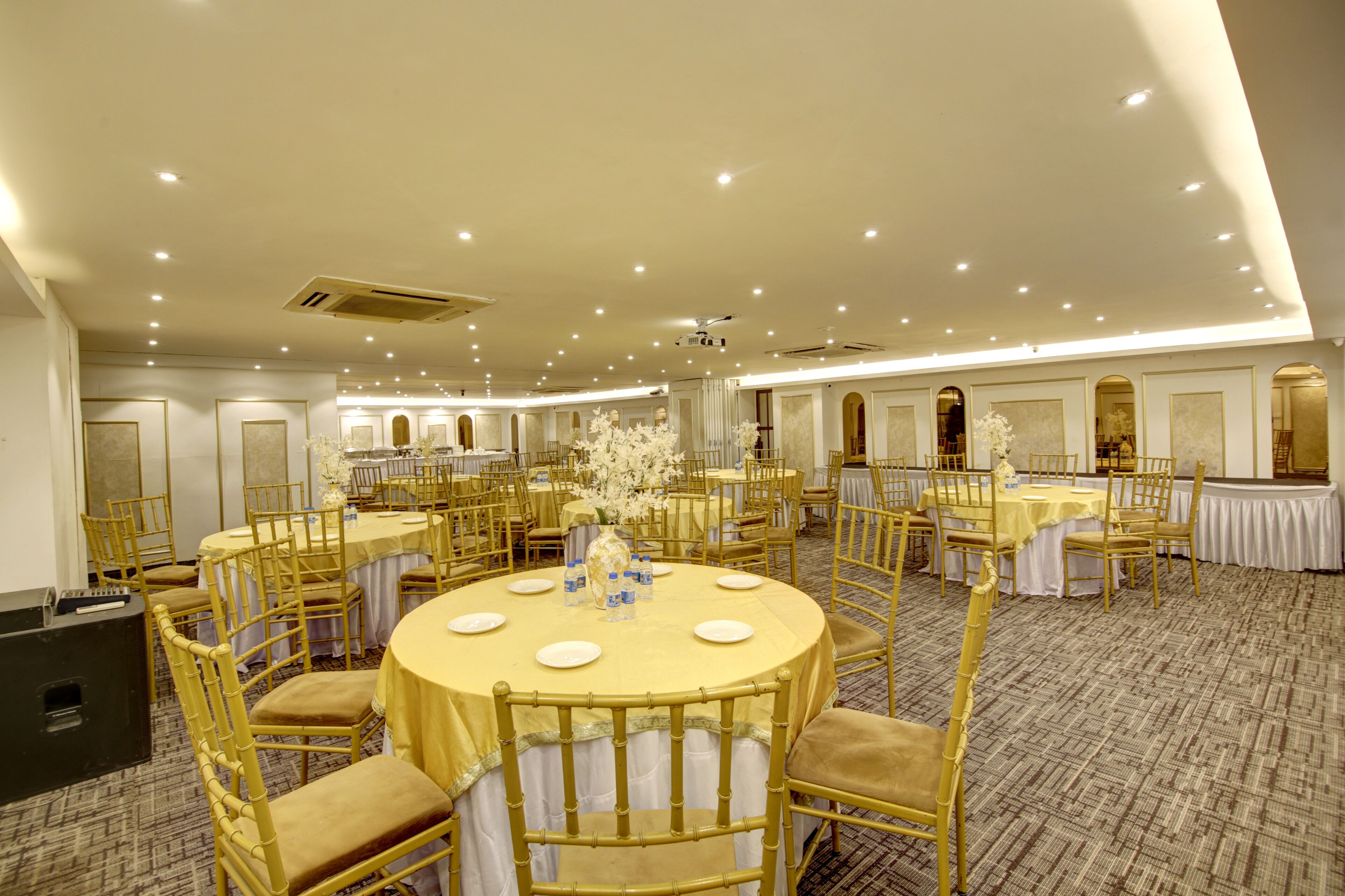 A banquet hall with round tables, gold chairs, and white drapery.