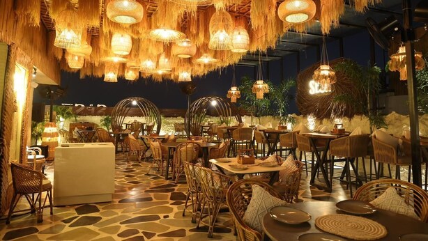 An outdoor dining area with wicker furniture, hanging wicker lamps, and a stone floor. - Town Pallace Inn (New Delhi)