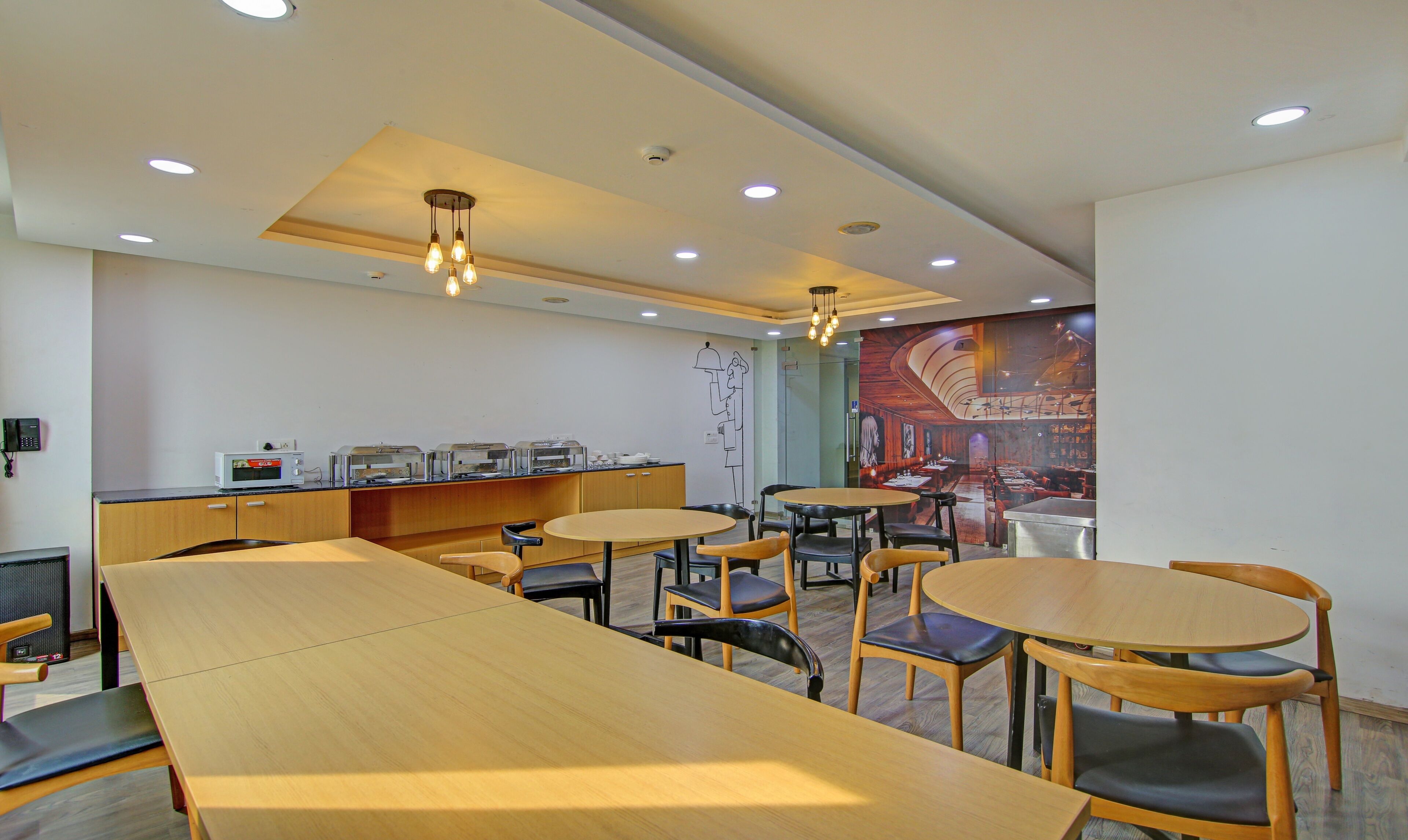 A modern restaurant with wooden tables and chairs, a kitchen area with appliances, and a mural on the wall.