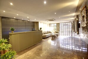 A reception area with a reception desk, a sofa, and a large window providing natural light. - Town Pallace Inn (New Delhi)