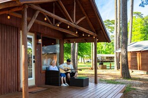 A wooden cabin with a porch, a dining area, and a view of the surrounding trees. - Rustic Cedar Waterfront Cabin 7 on Toledo Bend (Hemphill)