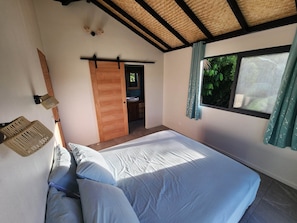 Ein Schlafzimmer mit einem großen Bett, einer Holztür, einem kleinen Badezimmer und einem Fenster mit Vorhängen.