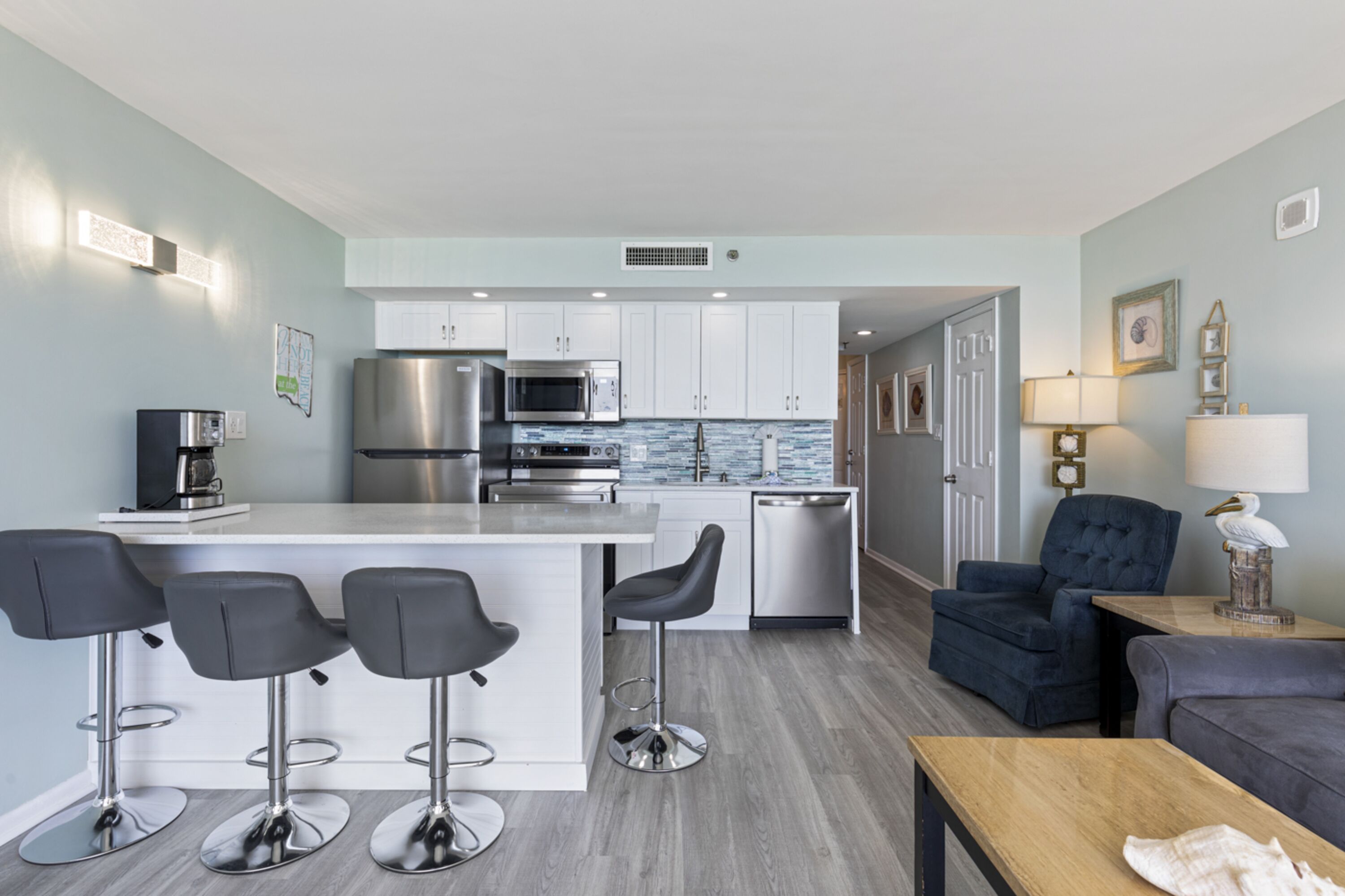A modern kitchen with white cabinets, stainless steel appliances, and a bar area with stools.